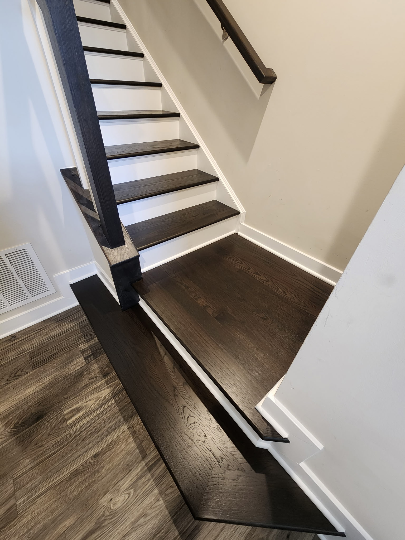 Front view of black-stained hardwood staircase with white risers and dark handrail