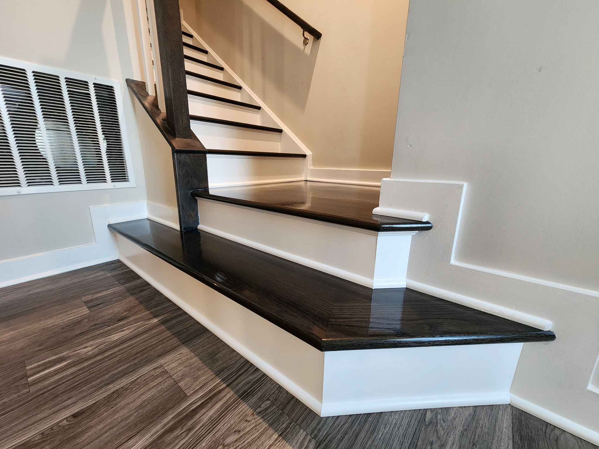Black-stained hardwood stair landing and lower steps with white risers